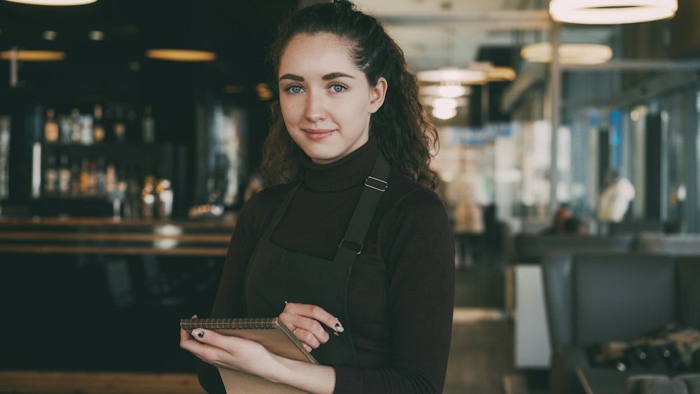 A restaurant employee holding a menu behind the counter.